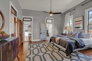 Une chambre à coucher avec un lit, un ventilateur de plafond, un tapis à motifs géométriques et une vue sur l’extérieur.