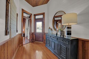 Un couloir aux murs lambrissés, une console en bois foncé agrémentée d’objets décoratifs et un grand miroir à cadre rond.