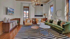 A modern living room with a checkered floor, a green sofa, a round coffee table, and a unique ceiling light fixture. - Luxury Stay Right Off Central Main St - Hot Tub! (Fredericksburg)