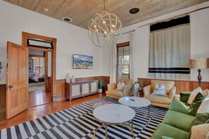 Un salon spacieux avec un tapis à carreaux, une table basse ronde, un canapé et une grande fenêtre avec des rideaux.