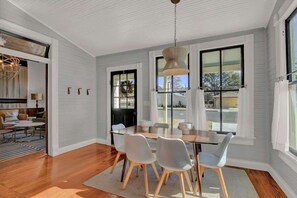 Un espace repas avec une table et des chaises en bois, de grandes fenêtres et un luminaire suspendu.