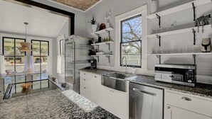 A modern kitchen with white cabinetry, granite countertops, a built-in oven, and a large window providing natural light. - Luxury Stay Right Off Central Main St - Hot Tub! (Fredericksburg)