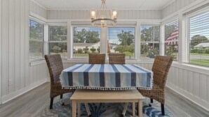 A covered dining area with a table and four wicker chairs, large windows, and a chandelier. - 2 for 1❗️2 separate houses (Pensacola)