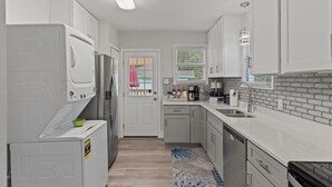 A modern kitchen with white cabinets, a dishwasher, a refrigerator, and a window with blinds. - 2 for 1❗️2 separate houses (Pensacola)