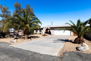 A residential driveway with a garage, palm trees, and a clear blue sky.