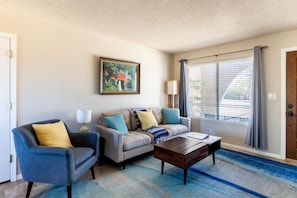 A living room with a sofa, armchair, coffee table, and a painting on the wall.