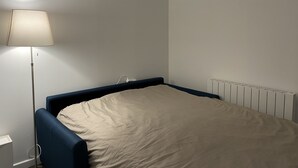 Een kleine kamer met een eenpersoonsbed, een blauw hoofdeinde, een nachtkastje en een lamp.