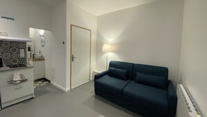 Een ruimtelijk ingerichte leefruimte met een kitchenette, een bank en een deur naar een andere kamer.