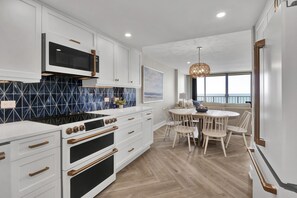 Una cocina moderna con armarios blancos, un microondas negro y una estufa. Hay un comedor con una mesa redonda y sillas.