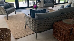 Ein großzügiges Wohnzimmer mit einem großen Schiebeglastür, die auf einen Balkon führt, Korbmöbeln und Blick auf den Strand.