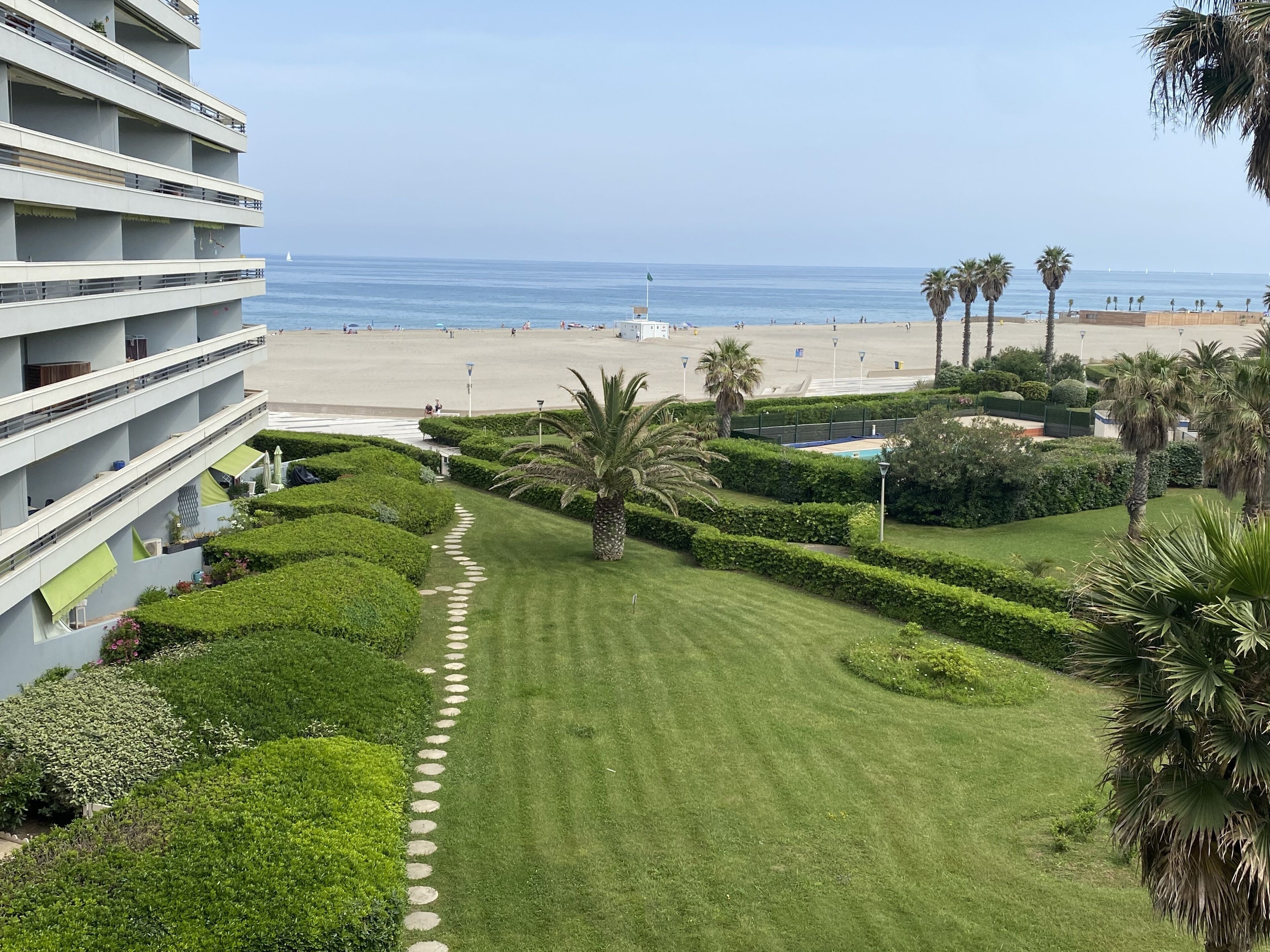 Un hôtel avec vue sur la plage, doté d’une pelouse bien entretenue, de palmiers et offrant une vue sur un ciel dégagé.