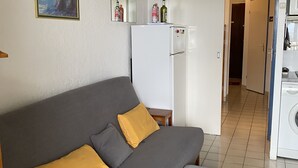 A living room with a grey sofa, yellow cushions, a small wooden table, a white refrigerator, and a painting on the wall. - T2 CABIN with terrace and exceptional sea view (Canet-en-Roussillon)