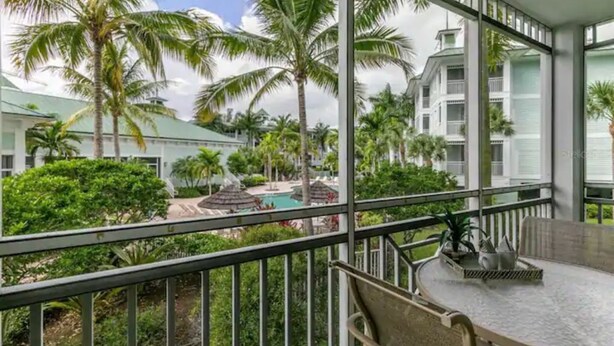 A balcony with a view of a pool, palm trees, and a building with a white facade. - Beautiful Resort in Quiet, Gated Community w Pool (Port Charlotte)