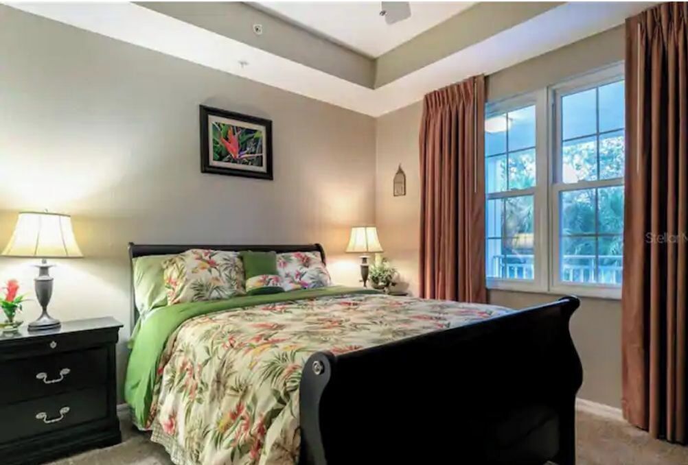 A bedroom with a bed, two bedside tables, a window with curtains, and a wall-mounted picture.
