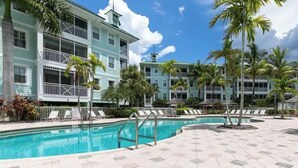 A pool area with a clear blue pool, palm trees, and a building with balconies. - Beautiful Resort in Quiet, Gated Community w Pool (Port Charlotte)