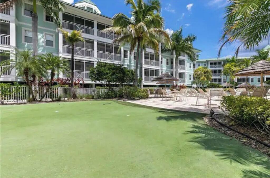 A hotel courtyard with a green lawn, palm trees, and outdoor seating areas.