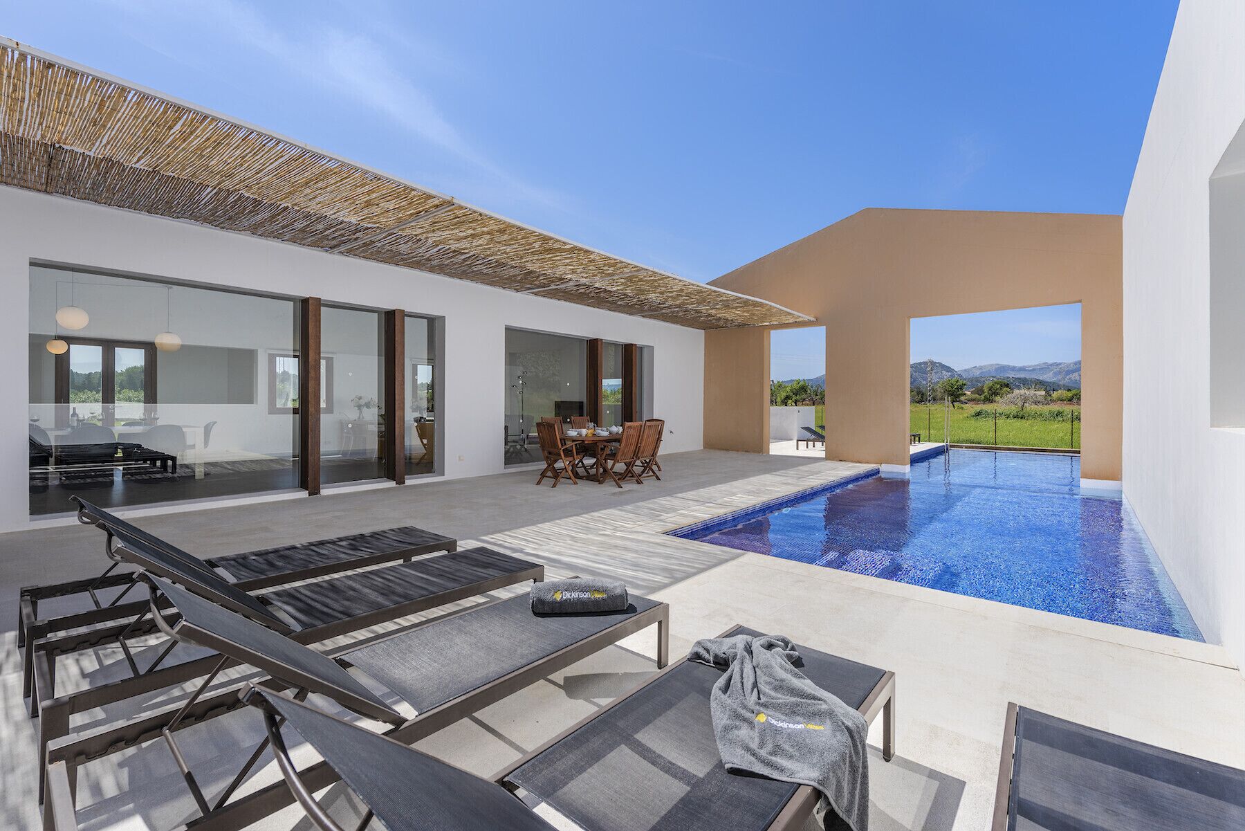 A modern outdoor pool area with lounge chairs, a dining table, and a view of the landscape.