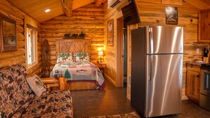 A log cabin interior with a wooden ceiling, a bed with a quilt, a sofa, a refrigerator, and a kitchen area. - The Ranch House Cabin at J&J Cabins (Salmon)