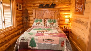 A cozy log cabin bedroom with a bed featuring a nature-themed quilt, a wooden headboard, and a mounted wall decoration of three horses. - The Ranch House Cabin at J&J Cabins (Salmon)