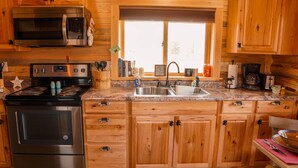 A kitchen with wooden cabinets, a stainless steel stove, a microwave, and a window above the sink. - The Ranch House Cabin at J&J Cabins (Salmon)