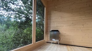 Una stanza con pareti e pavimento in legno, un'ampia finestra e un termosifone in metallo posizionato sul pavimento.