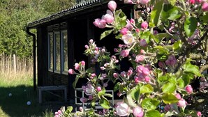 Una baita di legno con tetto spiovente, circondata da fiori rosa e bianchi in fiore.