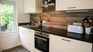 Una cucina moderna con mobili bianchi, un piano di lavoro nero, forno a incasso e una finestra vista verde.
