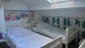 Une chambre de dortoir avec des lits superposés, un puits de lumière et un mur décoré d’objets sur le thème de la plage.