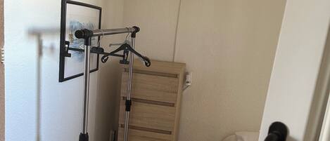 Une chambre à coucher comprenant un lit, une commode en bois, une étagère fixée au mur et un trépied.