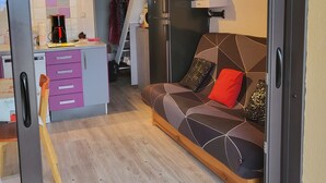 Un espace de vie compact comprenant un coin cuisine, un canapé agrémenté de coussins à motifs et un escalier menant à un niveau supérieur.