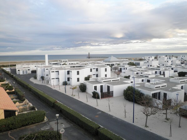 Un quartier résidentiel en bord de mer, avec des bâtiments modernes aux façades blanches, une plage en arrière-plan et un ciel dégagé.