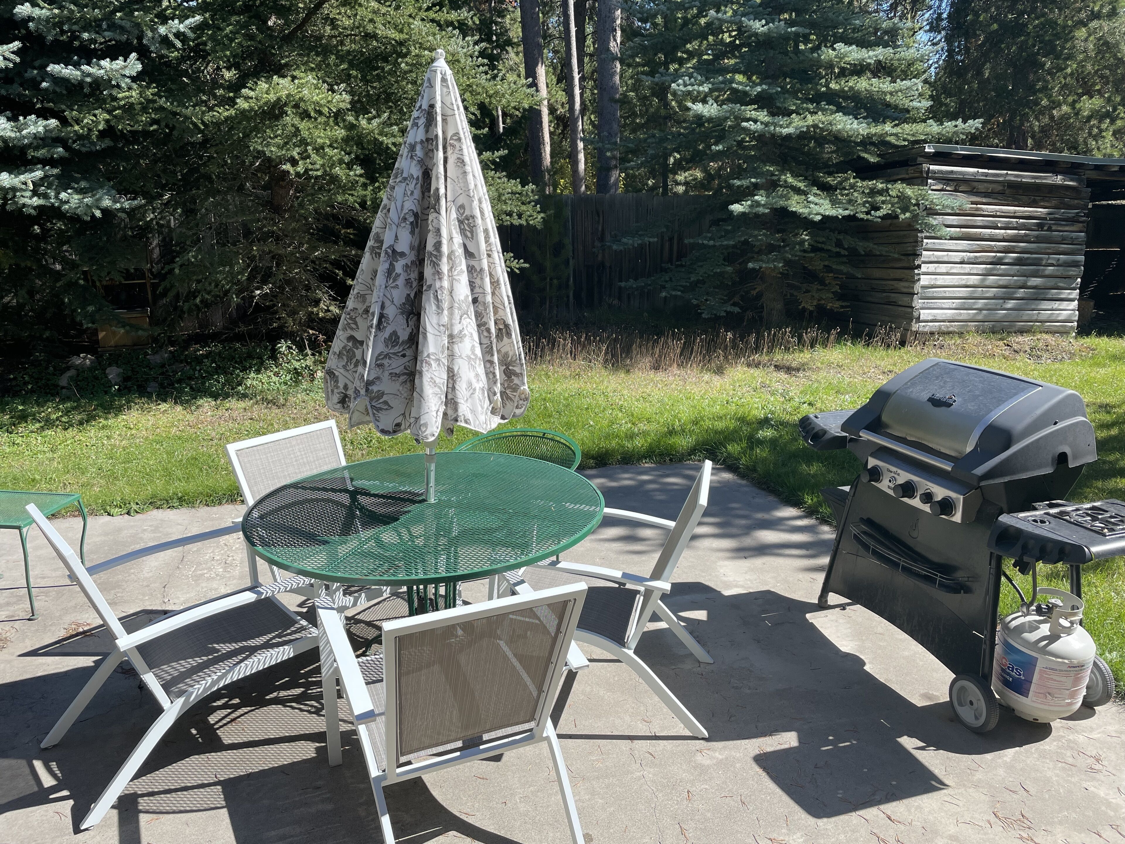 An outdoor patio with a round table, chairs, a grill, and a gas cylinder.