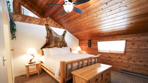 A wooden-paneled bedroom with a bed, bedside lamps, a wooden nightstand, and a ceiling fan.