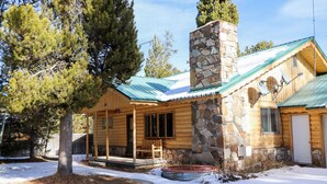 A log cabin with a stone chimney, wooden porch, and a snow-covered ground.