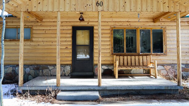 A wooden cabin with a stone foundation, a black front door, and a bench outside.