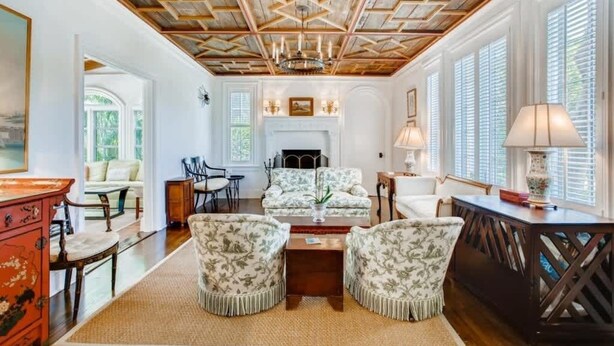A spacious living room with a high ceiling, a fireplace, and large windows.