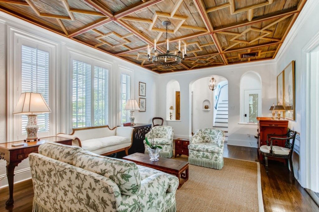 A spacious living room with a high ceiling, large windows, and classic furniture.