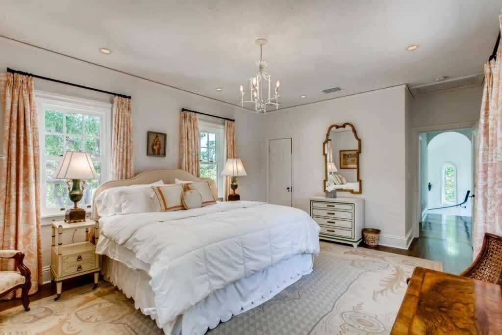 A bedroom with a large bed, bedside tables, a dresser, a mirror, and a chandelier.