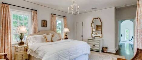 A bedroom with a large bed, bedside tables, a dresser, a mirror, and a chandelier.