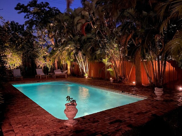 A rectangular swimming pool with a tiled border, surrounded by a brick patio.