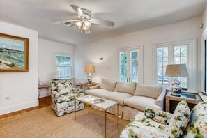 Una sala de estar con un sofá color beige, sillones estampados, una mesa de centro y un ventilador de techo.