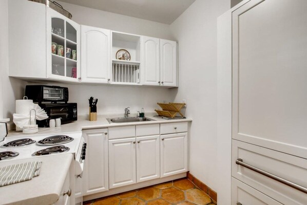 Una cocina compacta con muebles blancos, horno, pileta y microondas.
