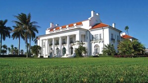 A large white building with a red roof, surrounded by palm trees and a well-maintained lawn. - Key Lime Cottage - Bask Poolside in a Historic Flamingo Park Gem (West Palm Beach)