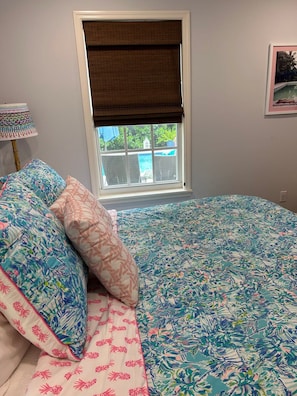 A bedroom with a large bed, a window with a view of a pool, and a lamp on a side table. - Key Lime Cottage - Bask Poolside in a Historic Flamingo Park Gem (West Palm Beach)