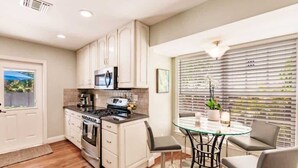 A modern kitchen with white cabinets, a stainless steel stove, and a glass dining table with chairs. - Key Lime Cottage - Bask Poolside in a Historic Flamingo Park Gem (West Palm Beach)
