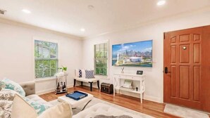 A modern living room with a sofa, coffee table, and a TV mounted on the wall. - Key Lime Cottage - Bask Poolside in a Historic Flamingo Park Gem (West Palm Beach)