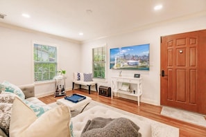 A living room with a sofa, a coffee table, a TV, and a wooden door. - Key Lime Cottage - Bask Poolside in a Historic Flamingo Park Gem (West Palm Beach)