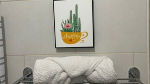 A bathroom with a white towel rack holding a folded towel, a framed picture of cacti and a 'Happy Day' sign, and a tiled wall. - Small and cozy apartment perfect for working (Bouvet Island)