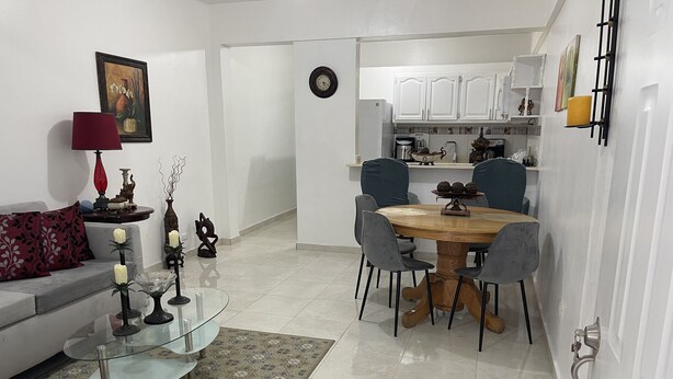 A modern living room with a glass coffee table, a dining area with a wooden table and chairs, and a kitchen with white cabinets. - Small and cozy apartment perfect for working (Bouvet Island)