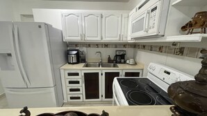 A compact kitchen with white cabinets, a stove, a sink, and a coffee maker. - Small and cozy apartment perfect for working (Bouvet Island)